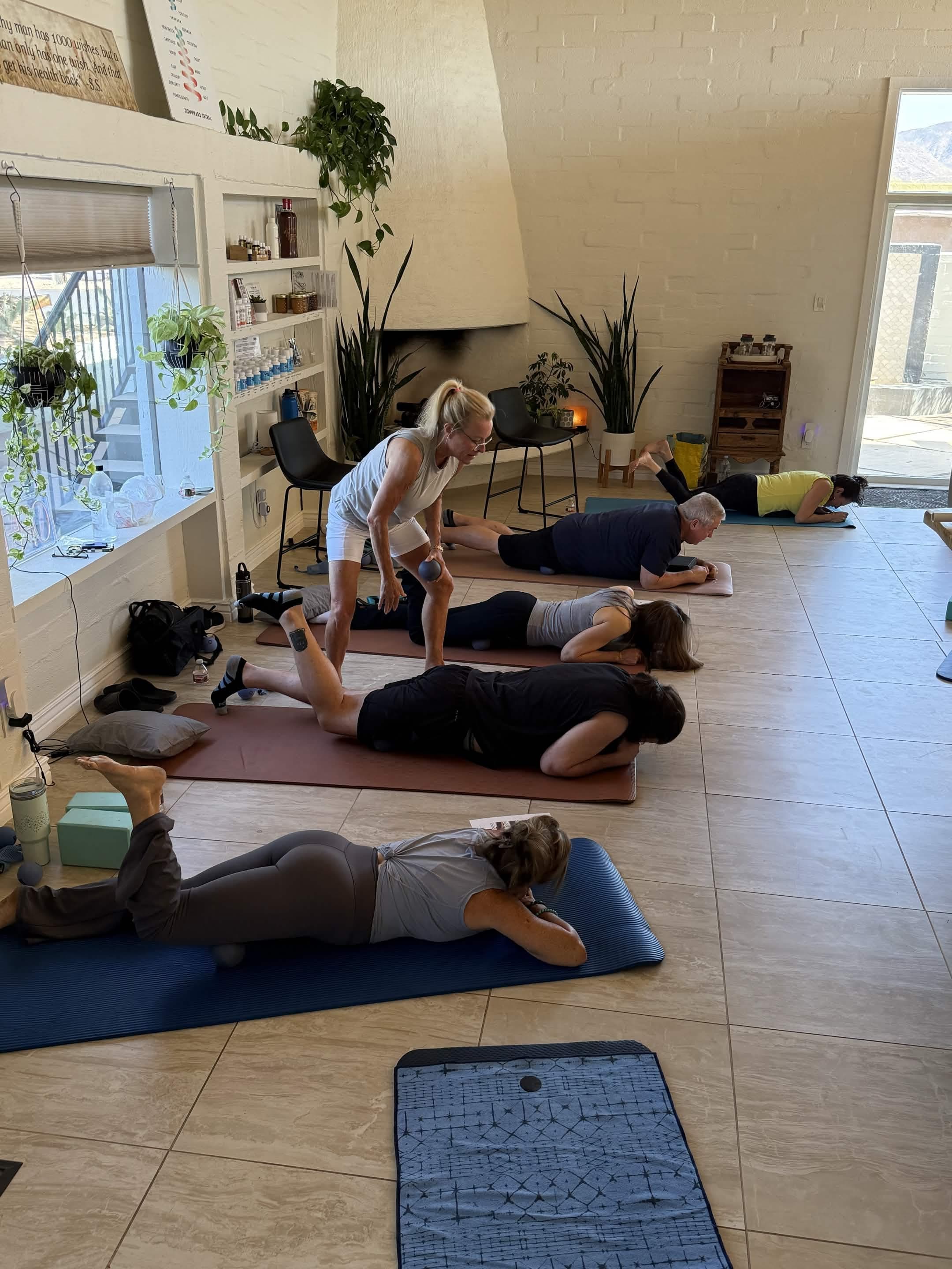 Instructor guides a small group through mat-based therapeutic movement exercises in a bright wellness studio.