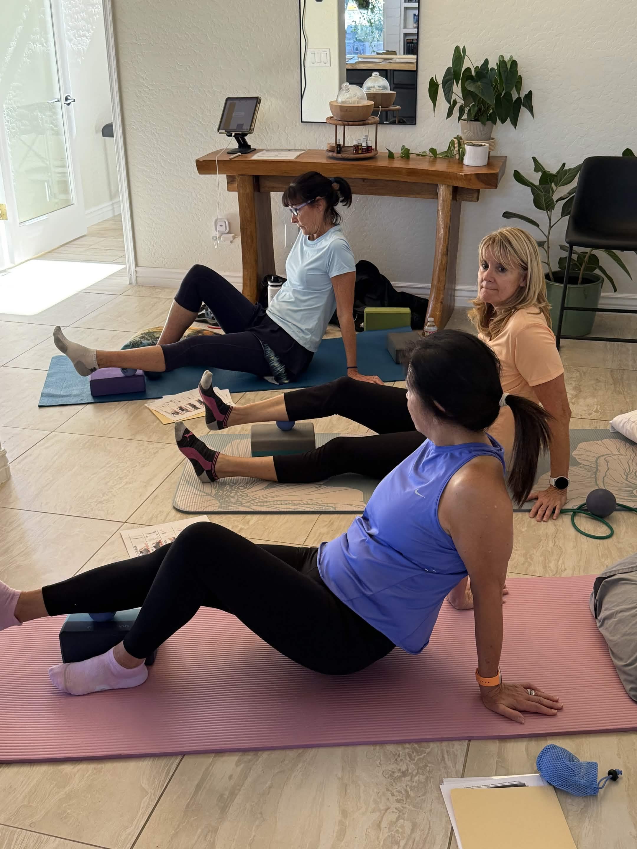 Small group seated on exercise mats using yoga blocks and massage balls during a wellness class.
