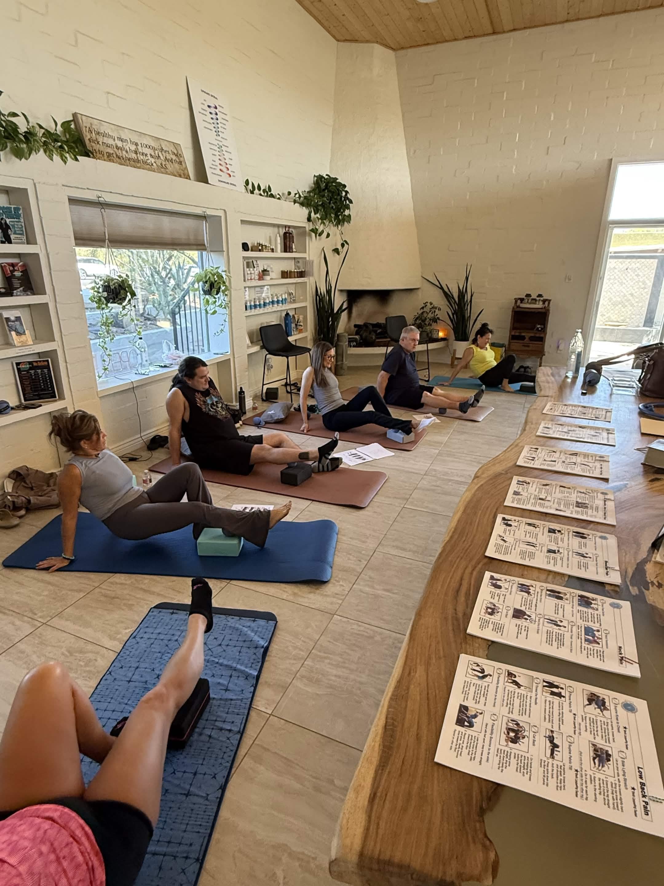 Participants practice therapeutic movement on mats in a bright wellness studio with plants and instructional handouts.